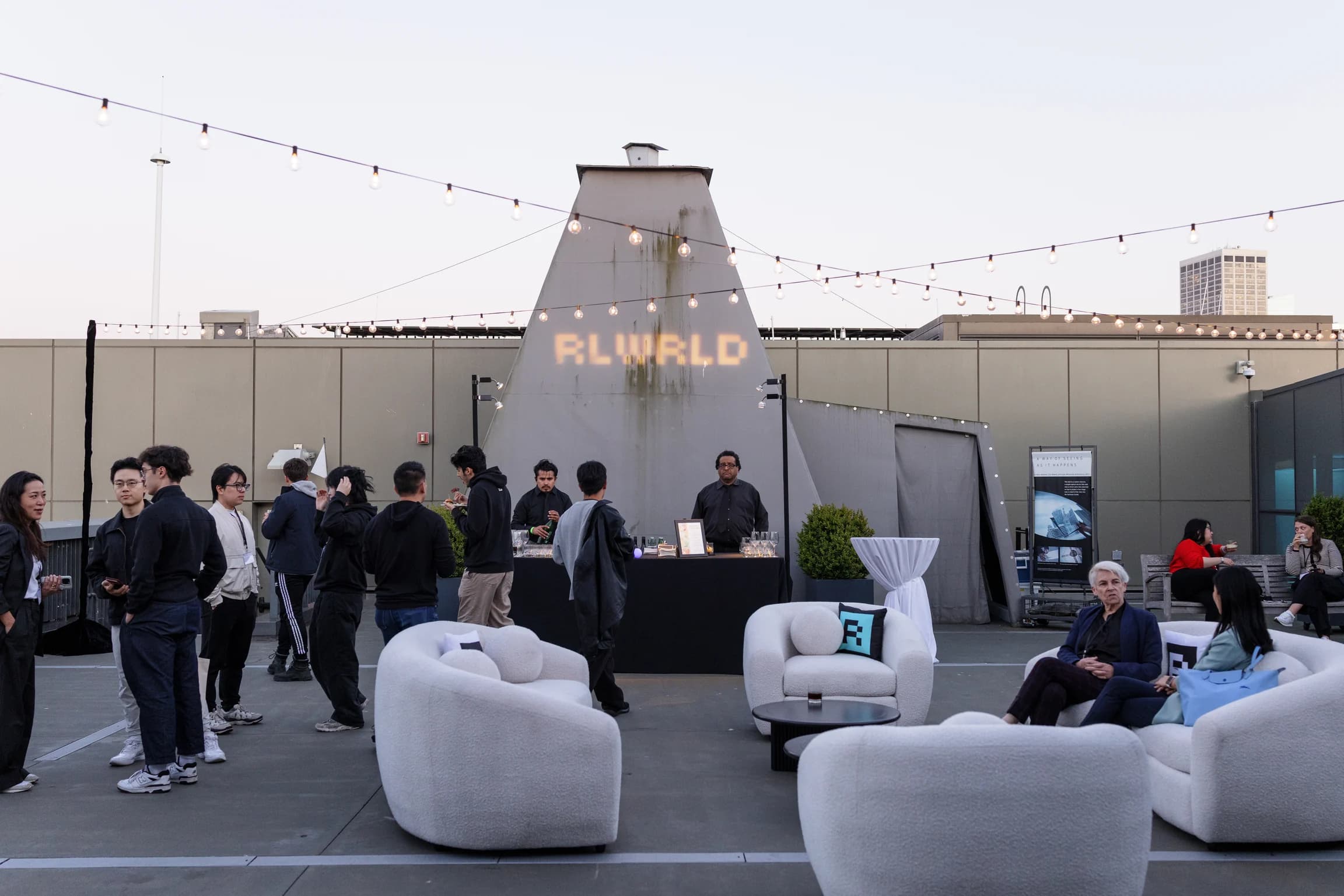 The terrace at dusk: RLWRLD projected on the Exploratorium cone over string lights, bar and lounge staged
