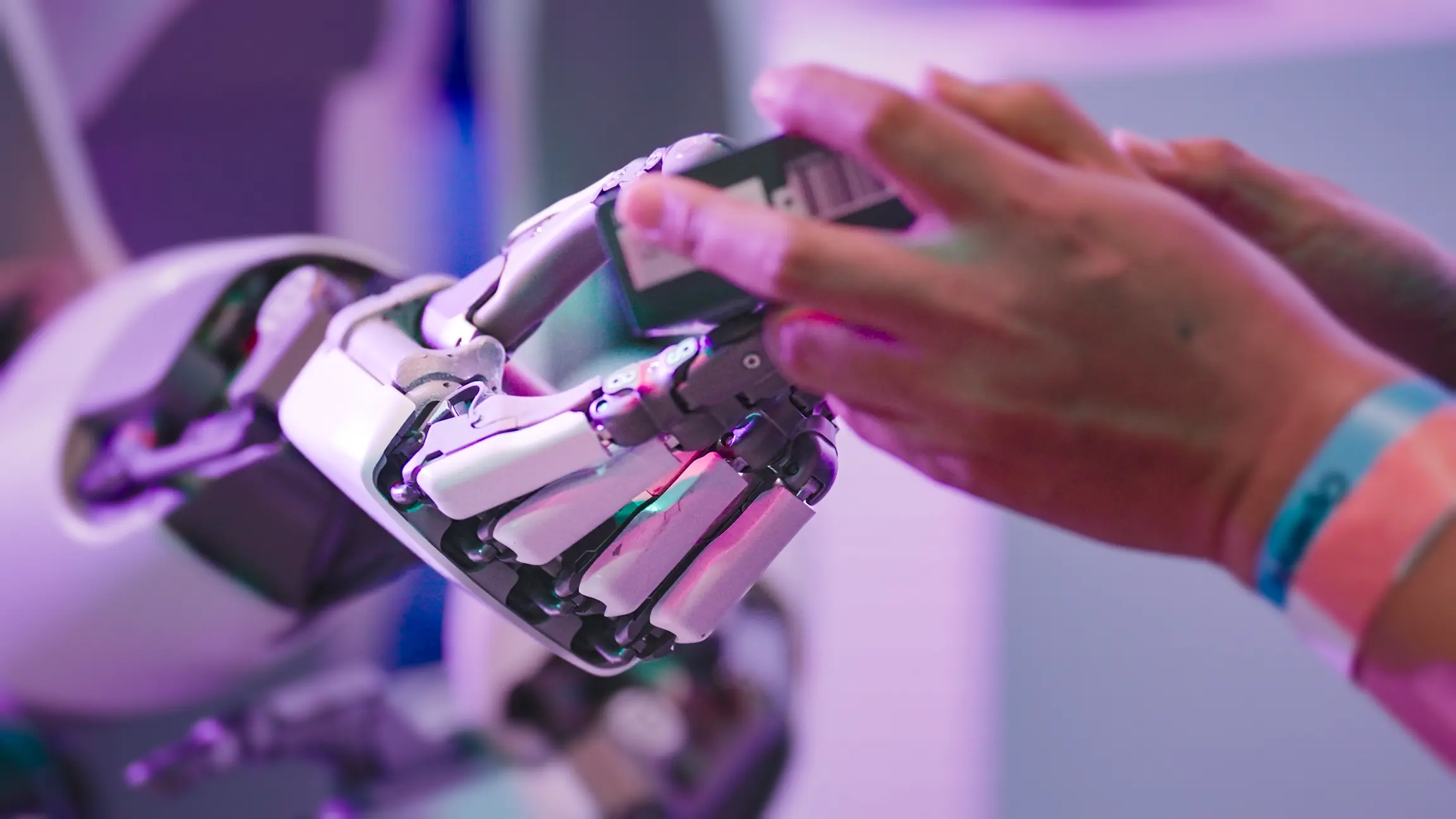 Human hand reaching toward the robot hand in pink and purple light